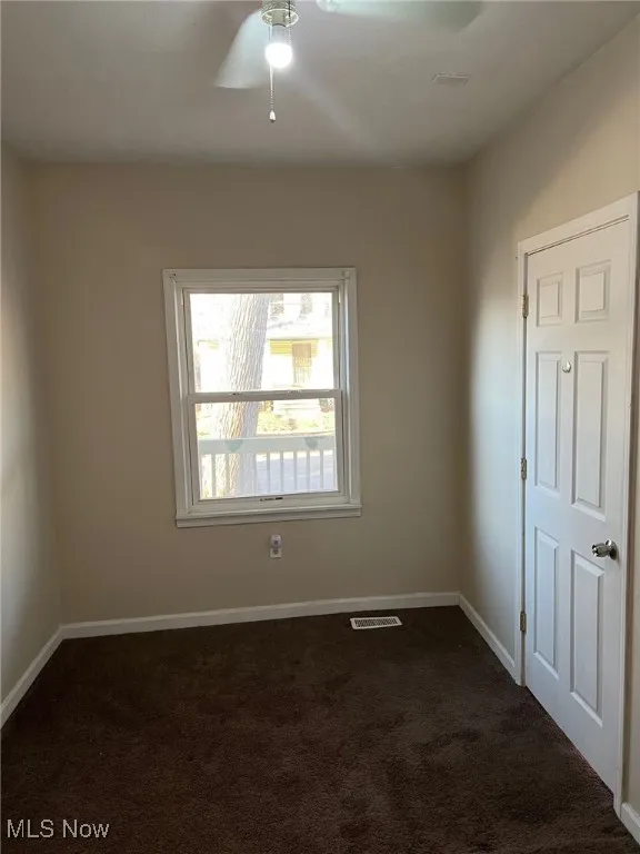 Empty room featuring ceiling fan, baseboards, dark colored carpet, and visible vents