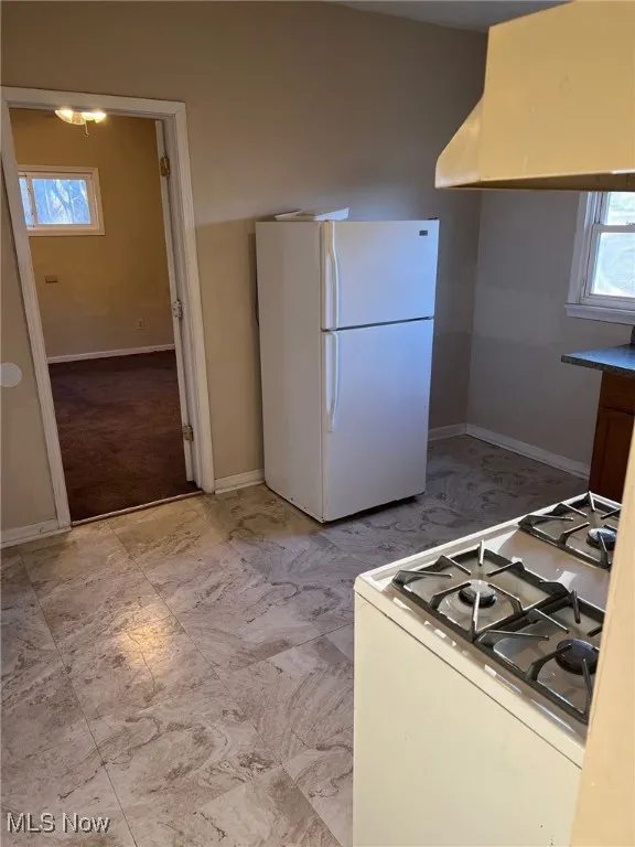 Kitchen featuring light countertops, baseboards, island range hood, and white appliances