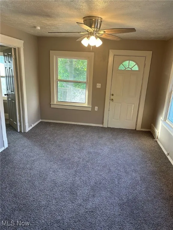 Entryway with a textured ceiling, dark carpet, and baseboards