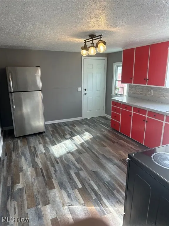 Kitchen with freestanding refrigerator, light countertops, dark wood finished floors, red cabinets, and range with electric stovetop