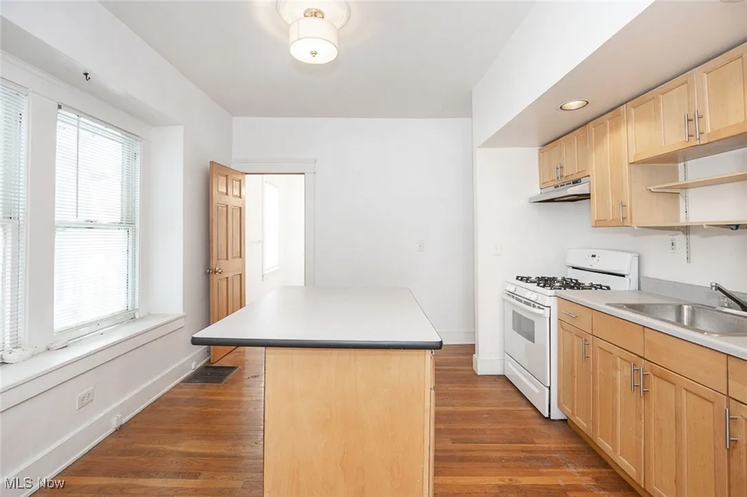 Kitchen featuring under cabinet range hood, a sink, a kitchen island, white range with gas cooktop, and light countertops