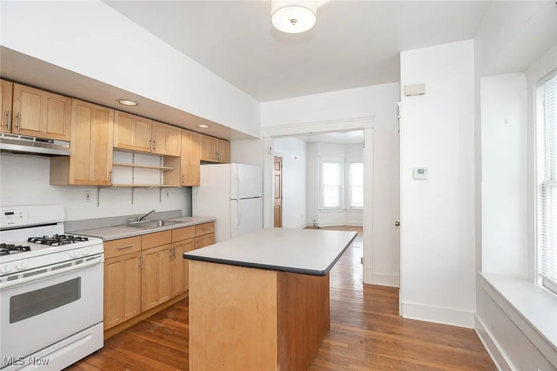 Kitchen with a center island, light countertops, a sink, white appliances, and under cabinet range hood