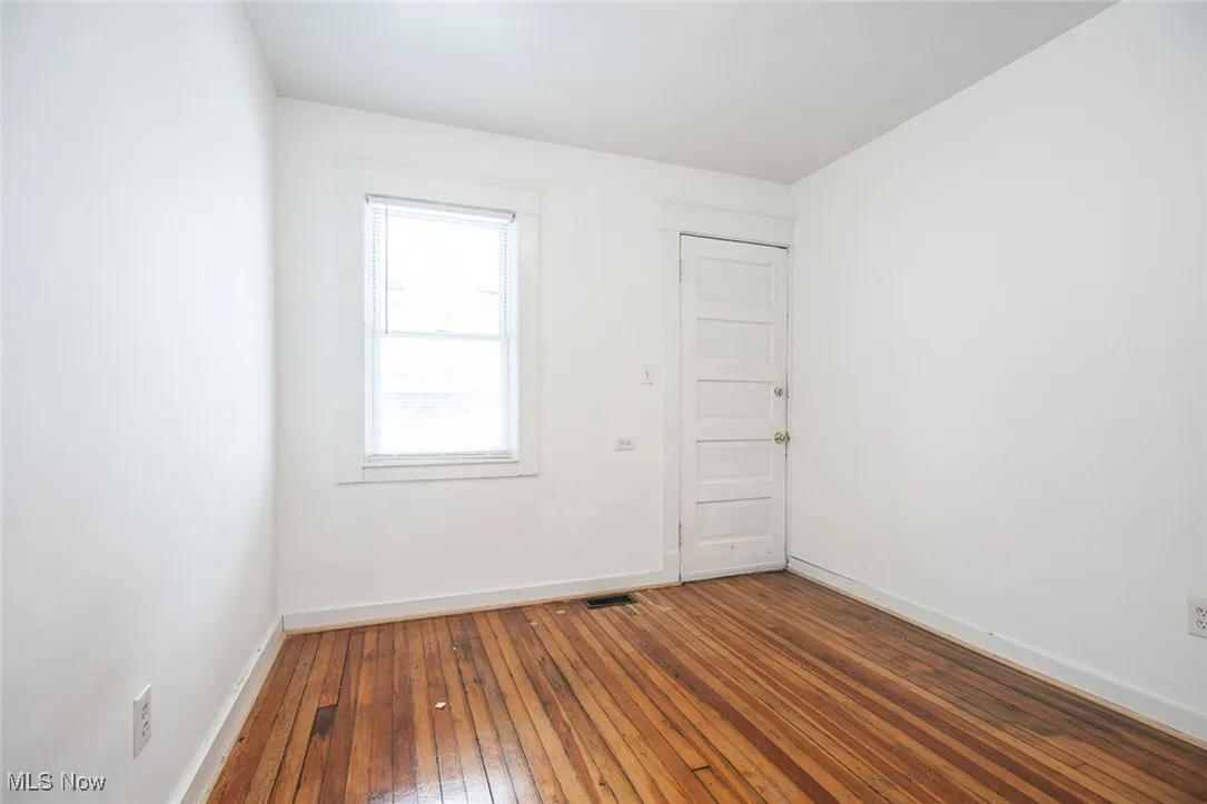 Empty room with dark wood-style floors, visible vents, and baseboards