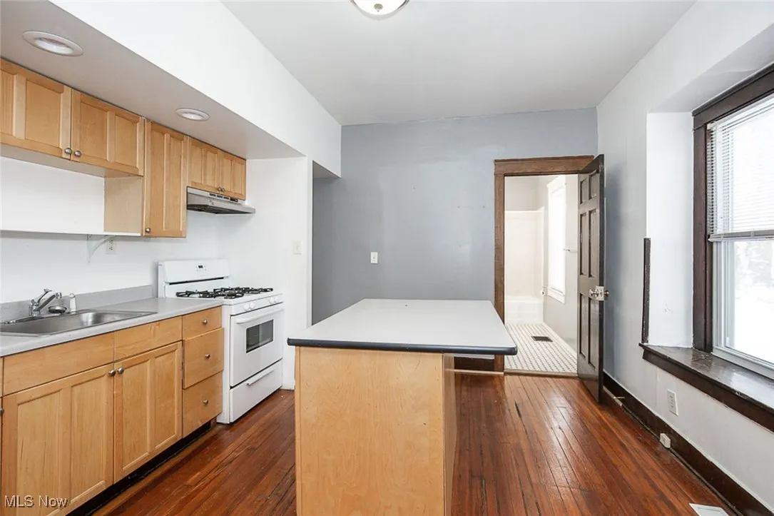 Kitchen with light countertops, white gas range oven, a sink, and under cabinet range hood