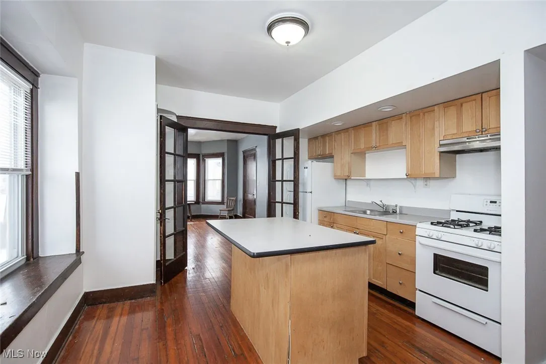 Kitchen featuring a center island, light countertops, a sink, white appliances, and under cabinet range hood