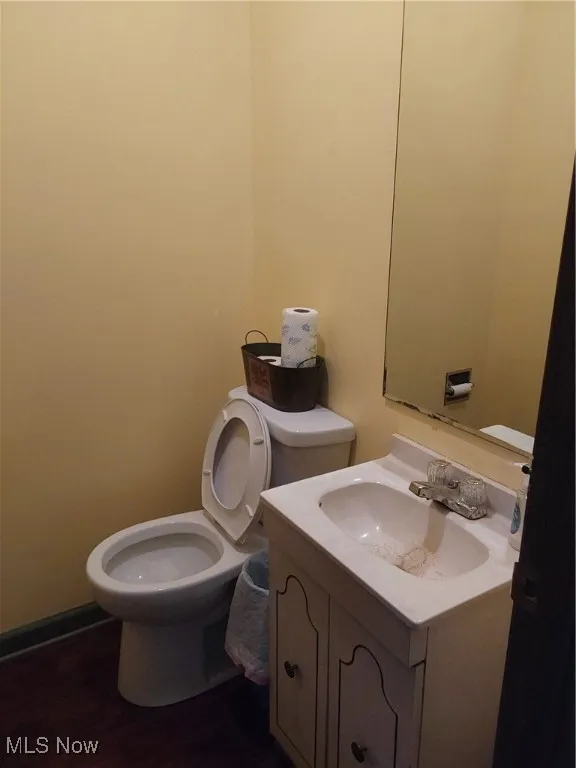 Half bath featuring toilet, wood finished floors, vanity, and baseboards