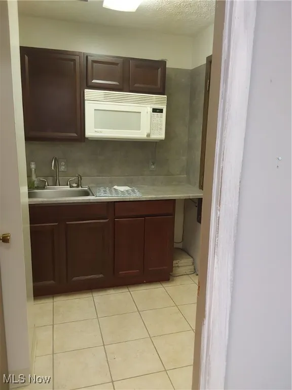 Kitchen featuring light countertops, a sink, a textured ceiling, and light tile patterned floors
