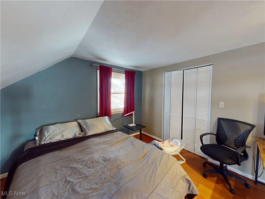 Bedroom featuring baseboards, wood finished floors, vaulted ceiling, a textured ceiling, and a closet