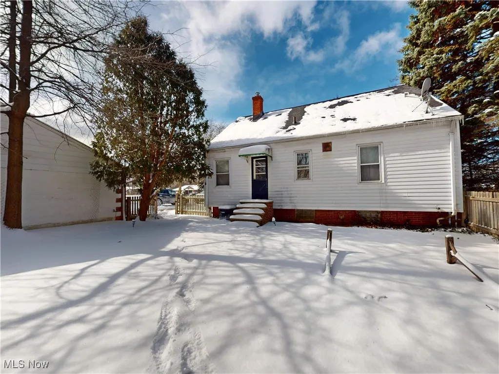 Snow covered property with entry steps, a chimney, and fence