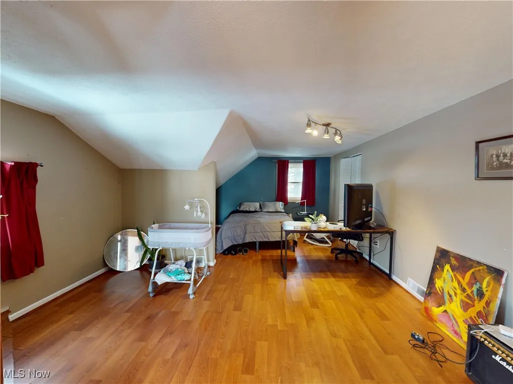 Bedroom with baseboards, visible vents, vaulted ceiling, and wood finished floors