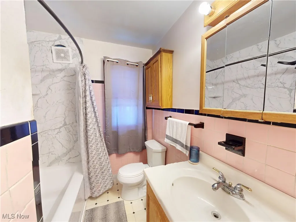 Bathroom with toilet, vanity, tile walls, and shower / bathtub combination with curtain