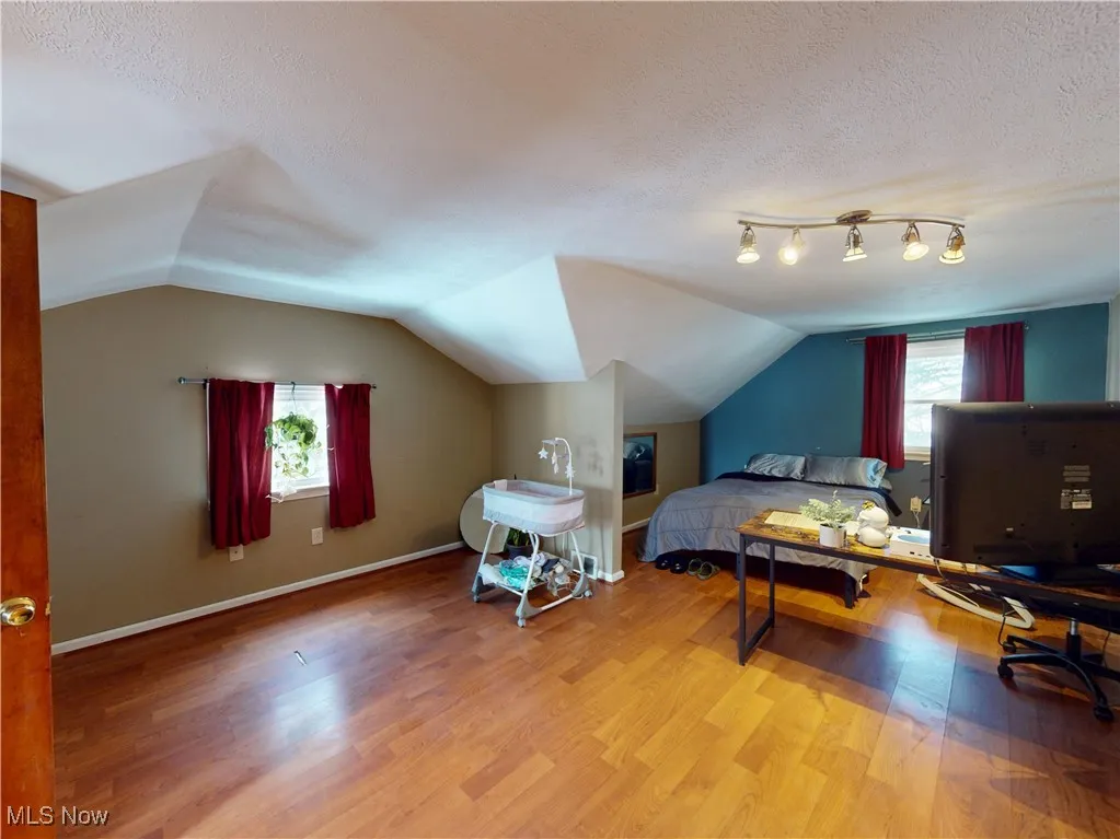 Bedroom with lofted ceiling, a textured ceiling, baseboards, and wood finished floors