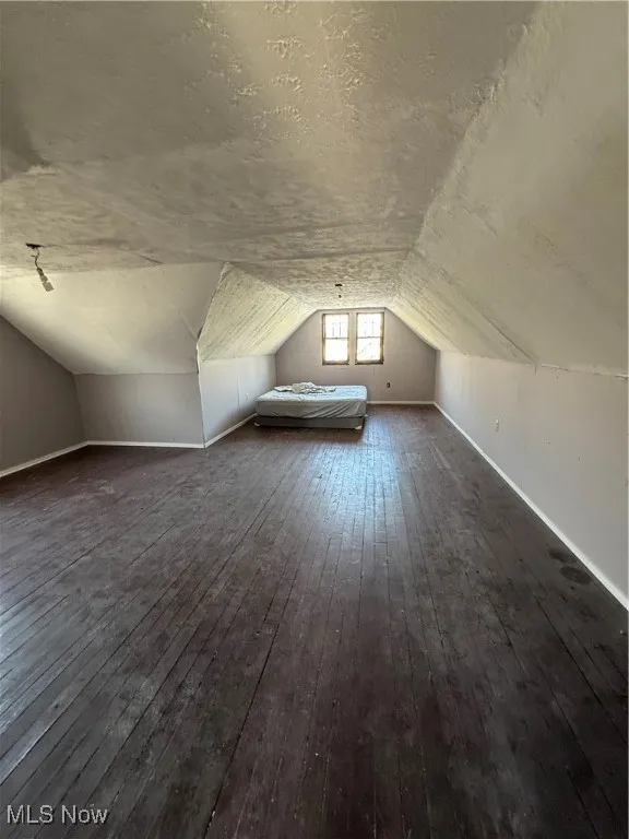 Bonus room featuring lofted ceiling, a textured ceiling, baseboards, and wood finished floors