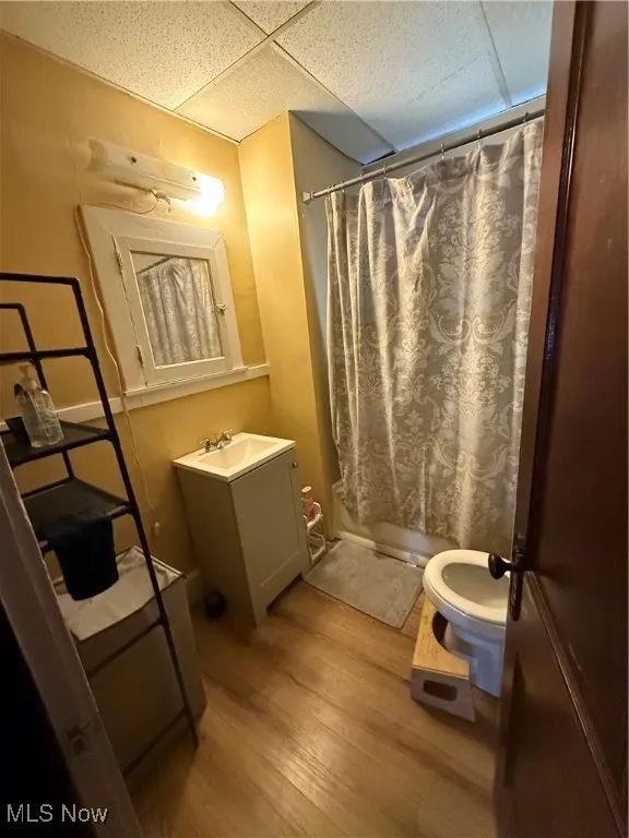 Bathroom with a drop ceiling, toilet, wood finished floors, vanity, and shower / bath combo