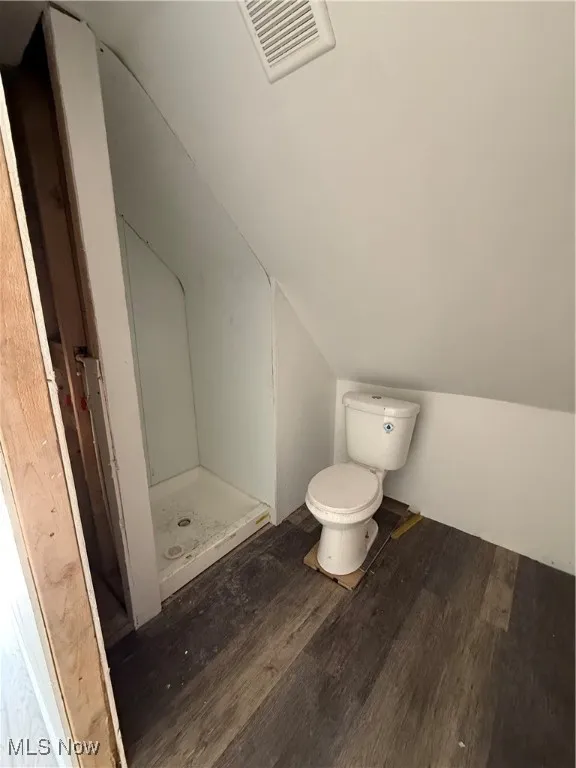 Bathroom featuring toilet, wood finished floors, visible vents, vaulted ceiling, and a shower stall