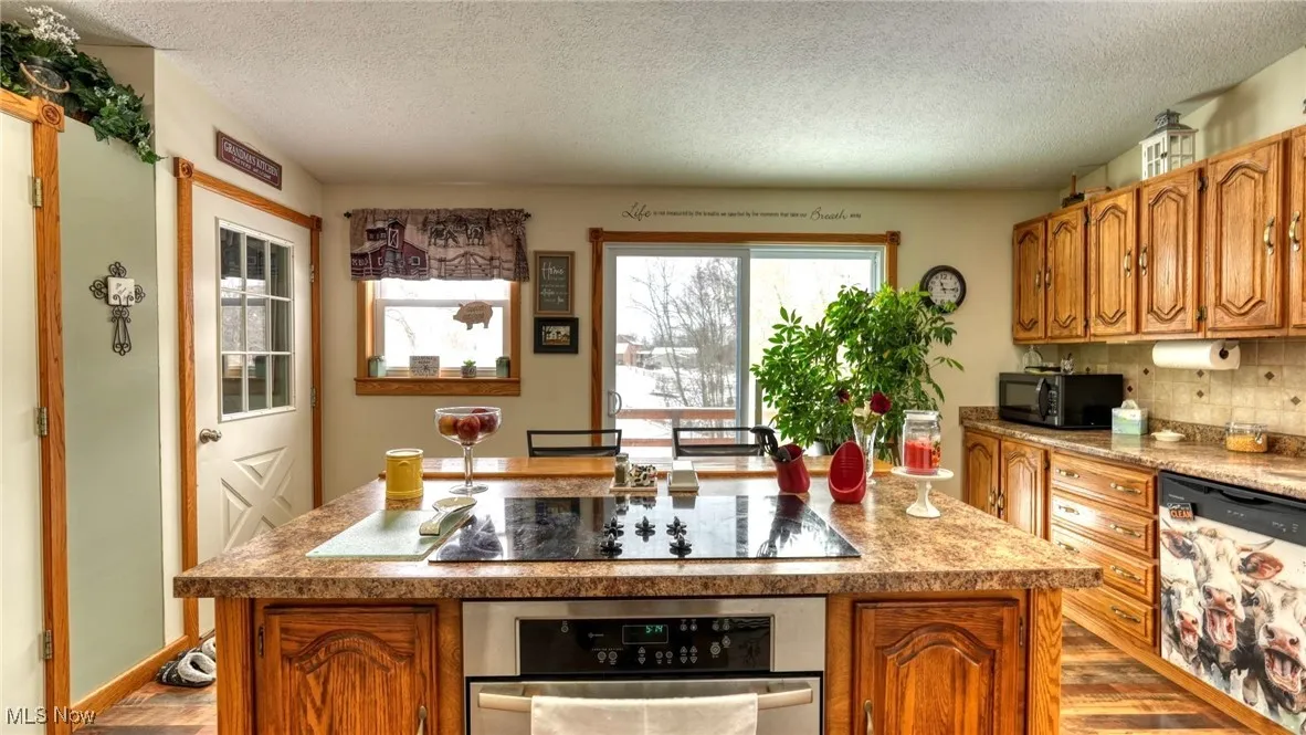 Kitchen with an island with sink, black appliances, light countertops, and brown cabinetry