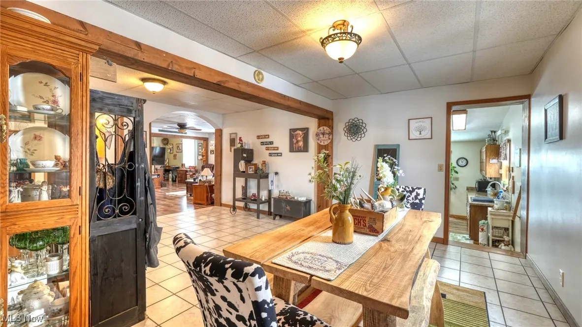 Dining room with light tile patterned floors, baseboards, arched walkways, a ceiling fan, and a drop ceiling