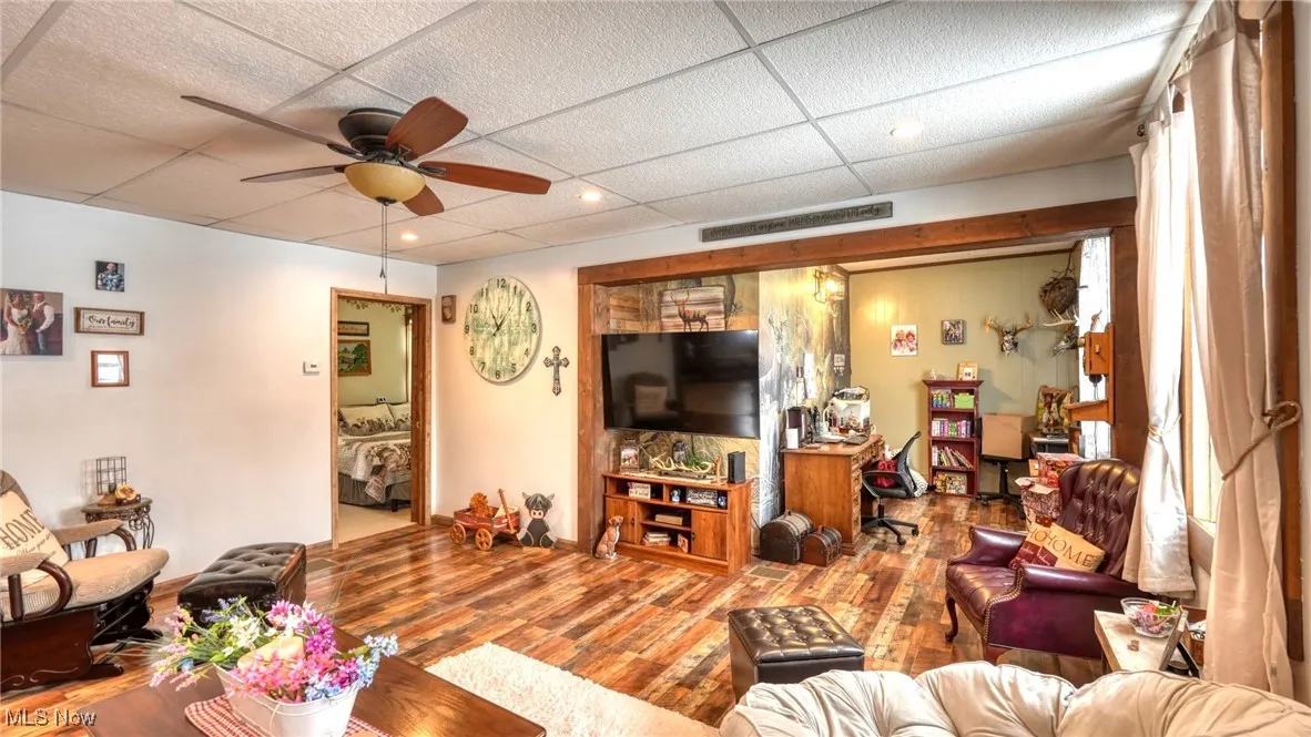 Living room featuring a drop ceiling, ceiling fan, and wood finished floors