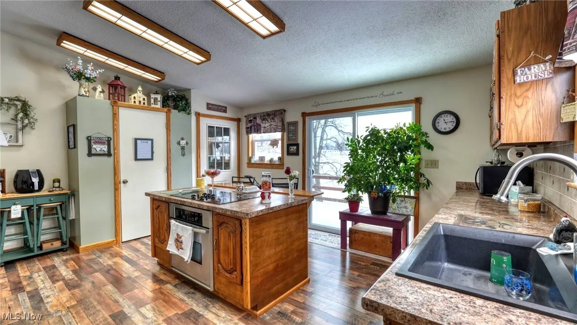 Kitchen with black electric cooktop, oven, dark wood-style flooring, a sink, and brown cabinets
