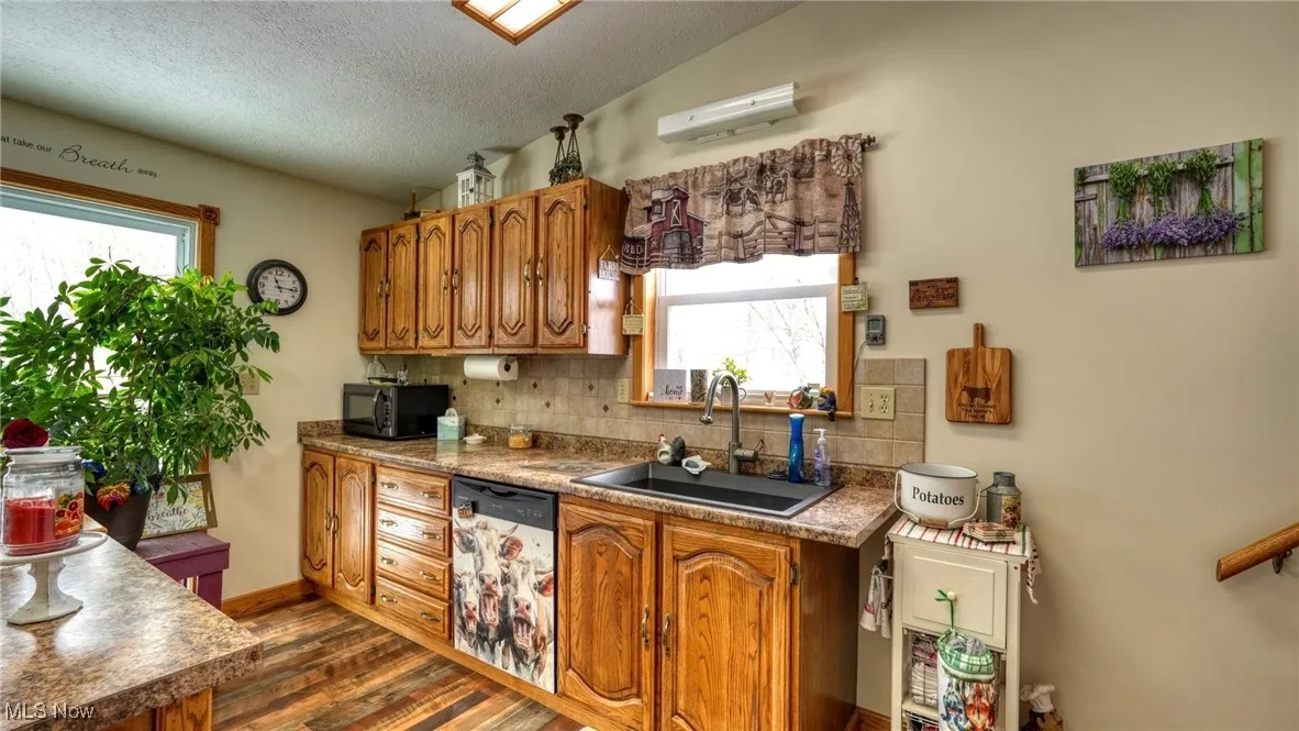 Kitchen featuring black microwave, a sink, vaulted ceiling, dishwasher, and brown cabinetry