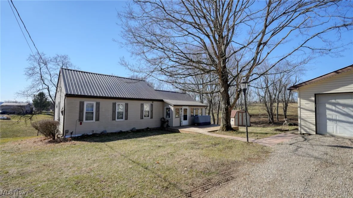 View of front of house with a front lawn, metal roof, a garage, an outdoor structure, and driveway