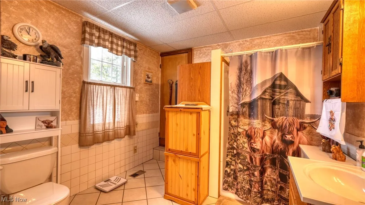 Bathroom with tiled walls, toilet, tile patterned flooring, and a drop ceiling