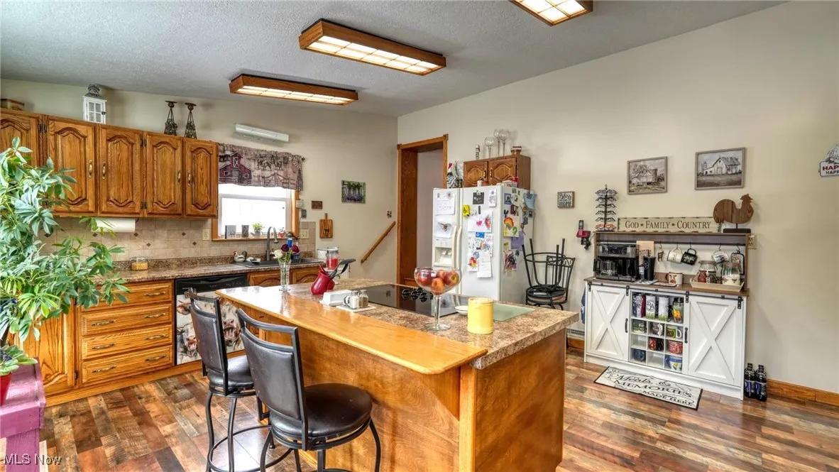 Kitchen with dark wood-style floors, white refrigerator with ice dispenser, light countertops, brown cabinetry, and a kitchen island