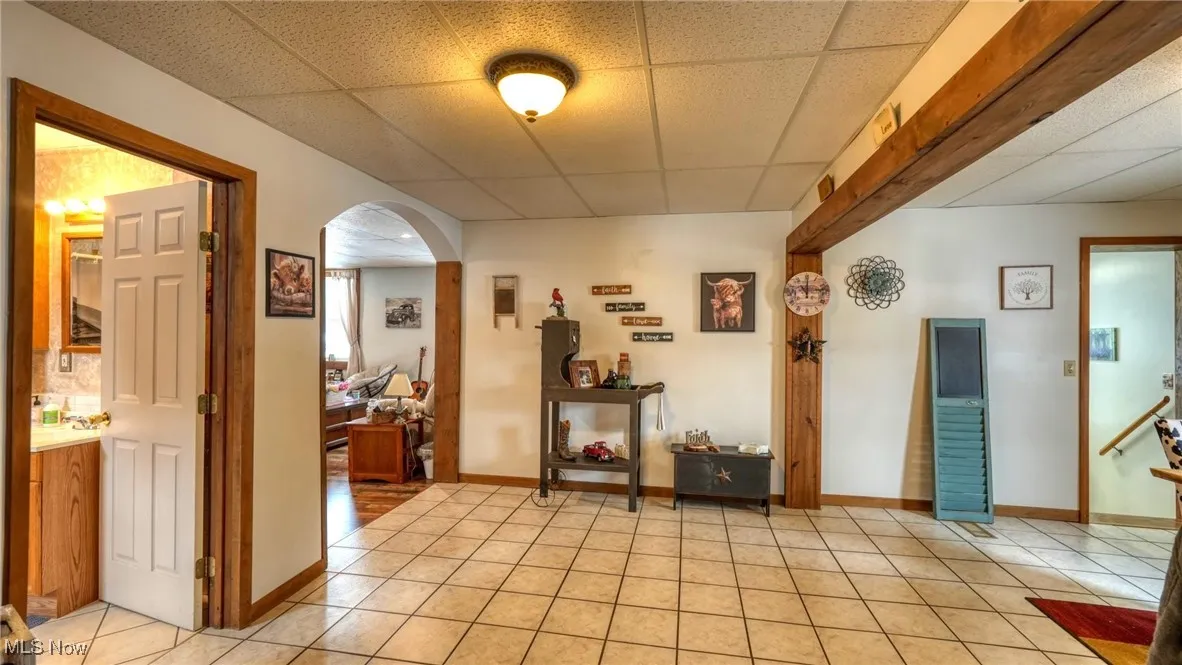 Corridor featuring light tile patterned floors, a drop ceiling, arched walkways, and baseboards
