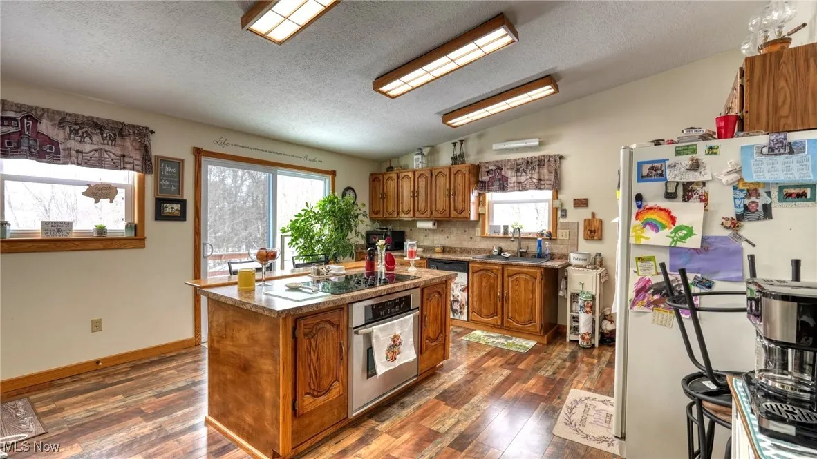Kitchen featuring brown cabinetry, freestanding refrigerator, vaulted ceiling, stainless steel oven, and a wealth of natural light