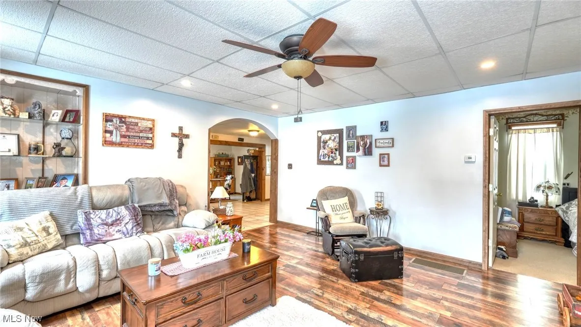 Living room featuring arched walkways, a drop ceiling, wood finished floors, and a ceiling fan