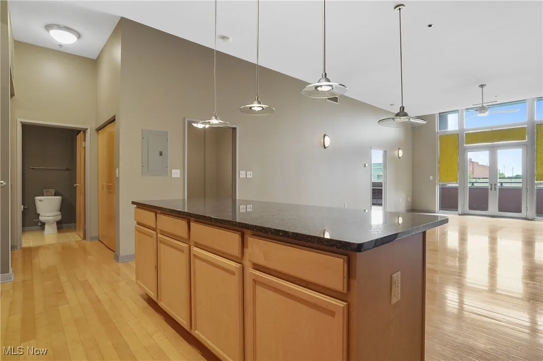 Kitchen featuring a towering ceiling, a kitchen island, light wood-type flooring, dark stone counters, and hanging light fixtures