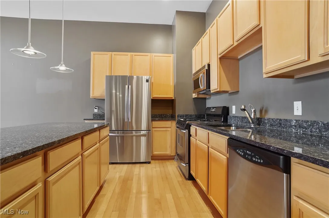 Kitchen with appliances with stainless steel finishes, light brown cabinetry, light wood finished floors, and dark stone countertops