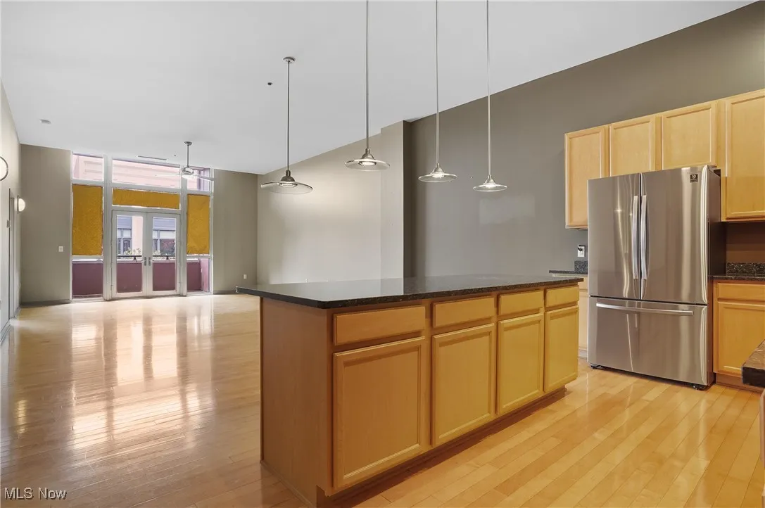 Kitchen with freestanding refrigerator, light wood finished floors, a center island, light brown cabinetry, and hanging light fixtures