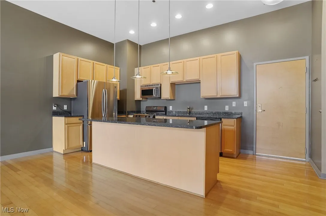 Kitchen featuring light brown cabinets, stainless steel appliances, light wood-style floors, a high ceiling, and a center island