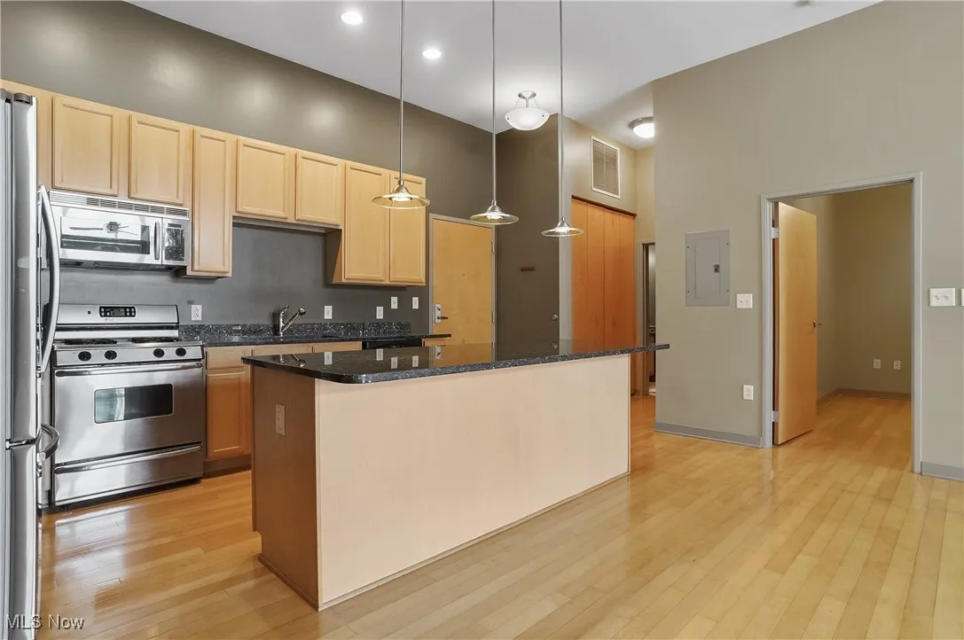 Kitchen featuring appliances with stainless steel finishes, light brown cabinetry, light wood-type flooring, a center island, and dark stone countertops