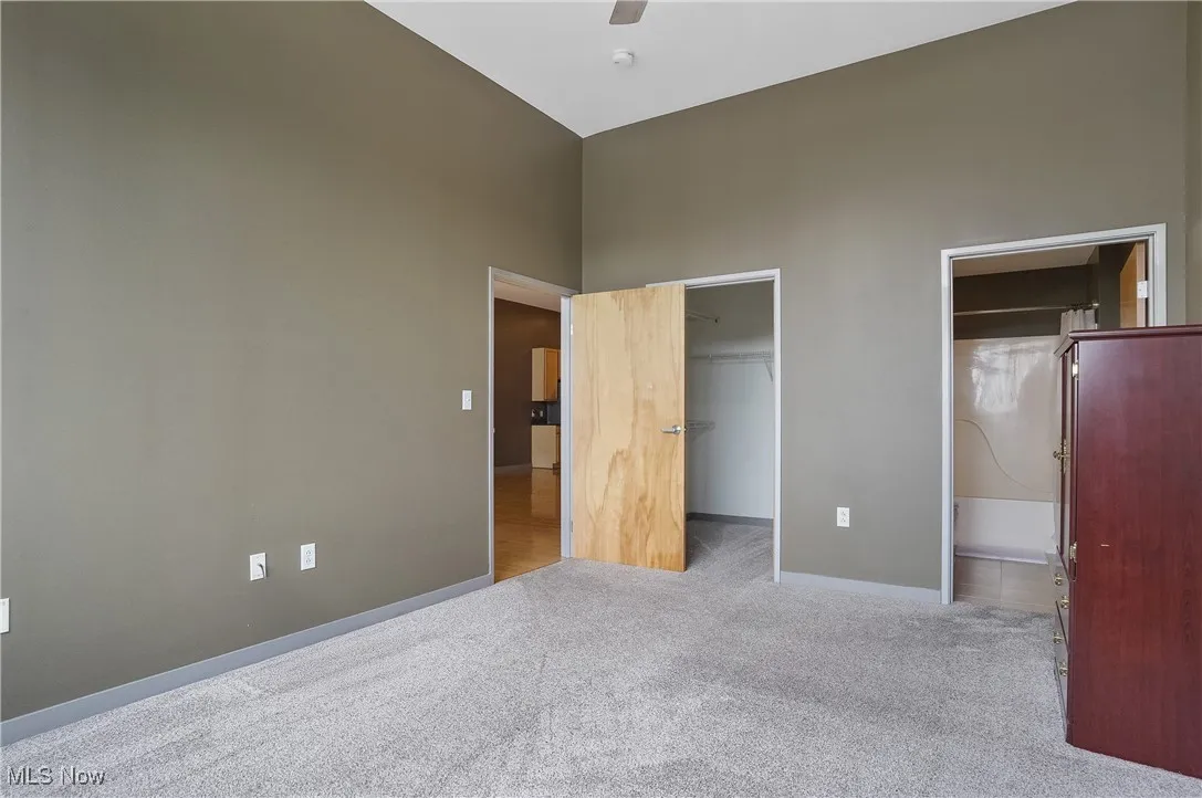 Unfurnished bedroom with carpet floors, a towering ceiling, a spacious closet, and a ceiling fan