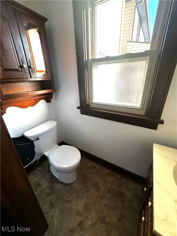 Bathroom with toilet, stone finish flooring, baseboards, and vanity
