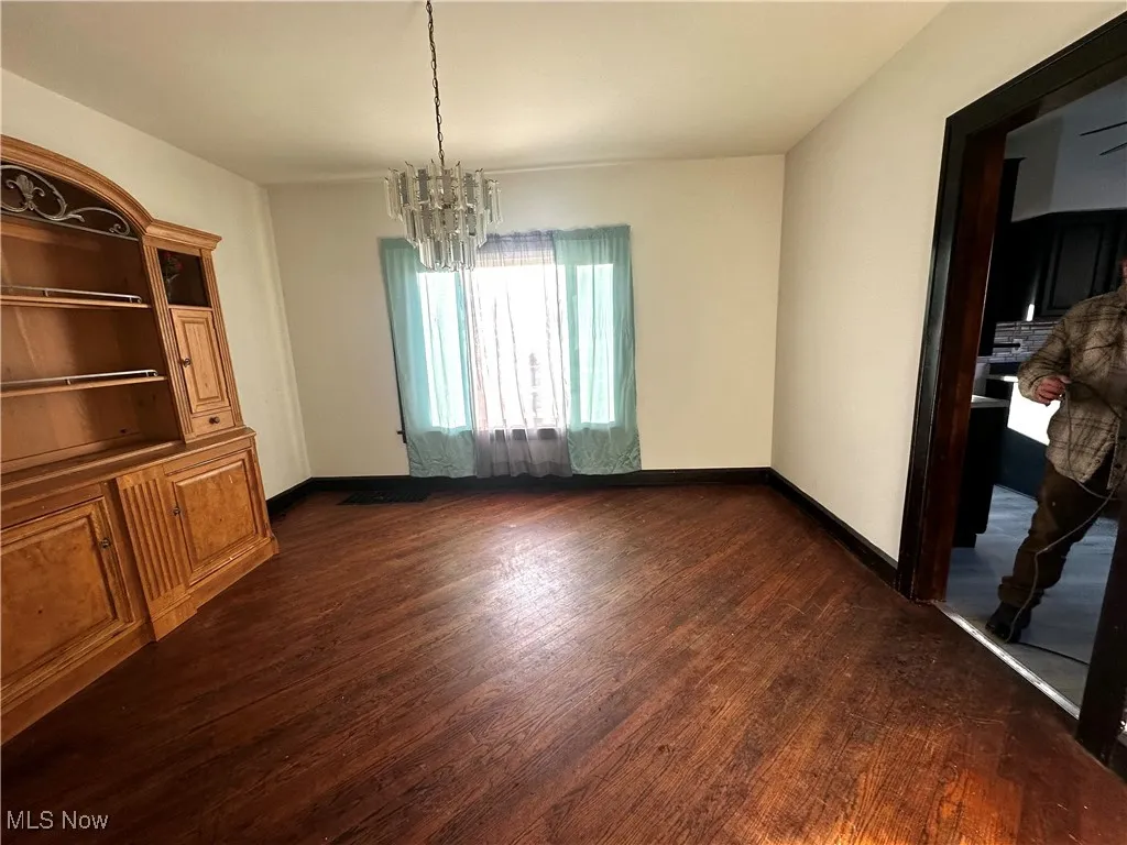 Unfurnished dining area with a chandelier, dark wood finished floors, and baseboards