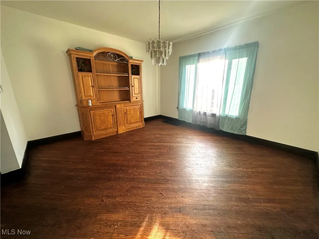 Unfurnished dining area with dark wood-style floors, baseboards, and a notable chandelier