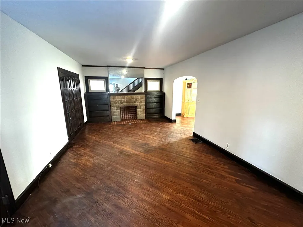 Unfurnished living room with visible vents, arched walkways, dark wood finished floors, baseboards, and a stone fireplace