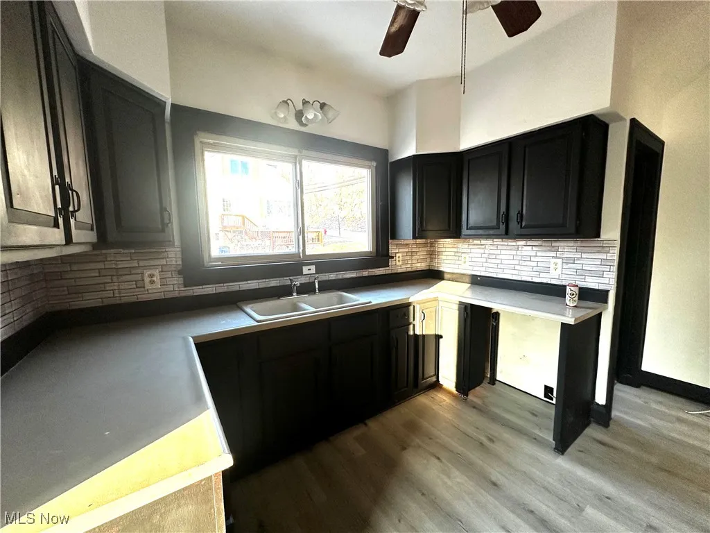 Kitchen with decorative backsplash, a ceiling fan, dark cabinets, light wood-style floors, and a sink