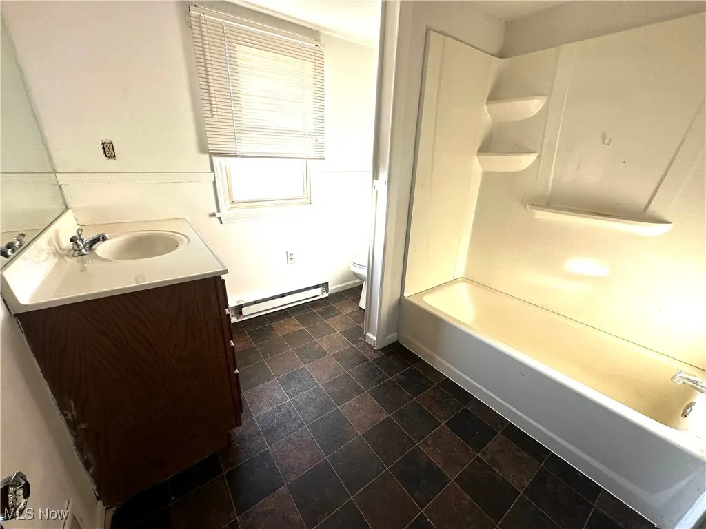 Bathroom with toilet, shower / tub combination, stone finish floor, baseboard heating, and vanity