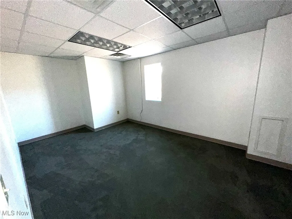 Spare room with dark colored carpet, a drop ceiling, visible vents, and baseboards