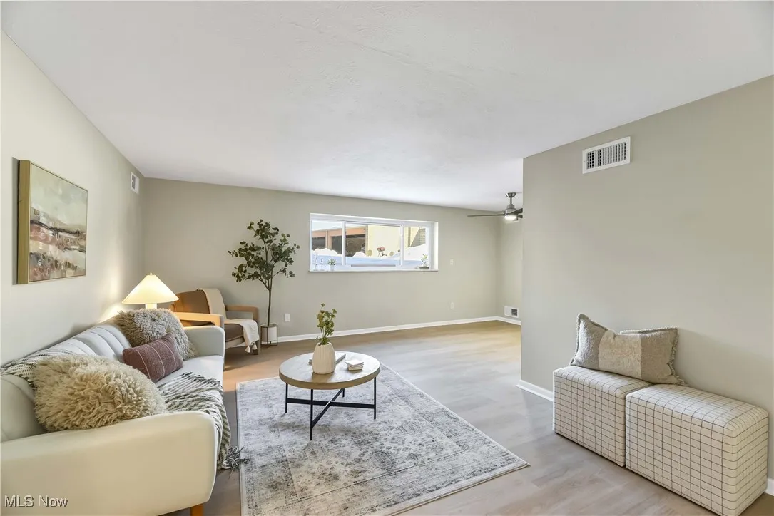 Living room featuring light wood-type flooring, visible vents, ceiling fan, and baseboards