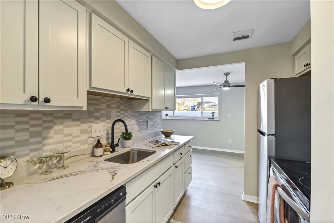 Kitchen featuring light stone counters, stainless steel appliances, visible vents, decorative backsplash, and a sink