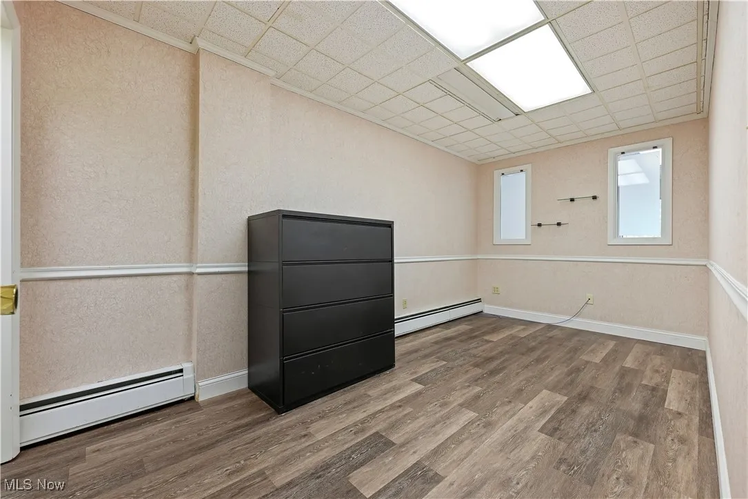 Empty room with a baseboard radiator, wood finished floors, a drop ceiling, and a textured wall