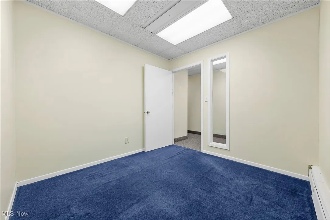 Carpeted spare room with a baseboard radiator and a drop ceiling