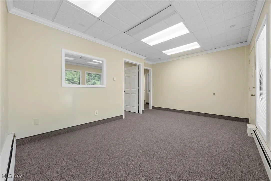 Empty room with baseboard heating, a baseboard heating unit, carpet flooring, ornamental molding, and a drop ceiling