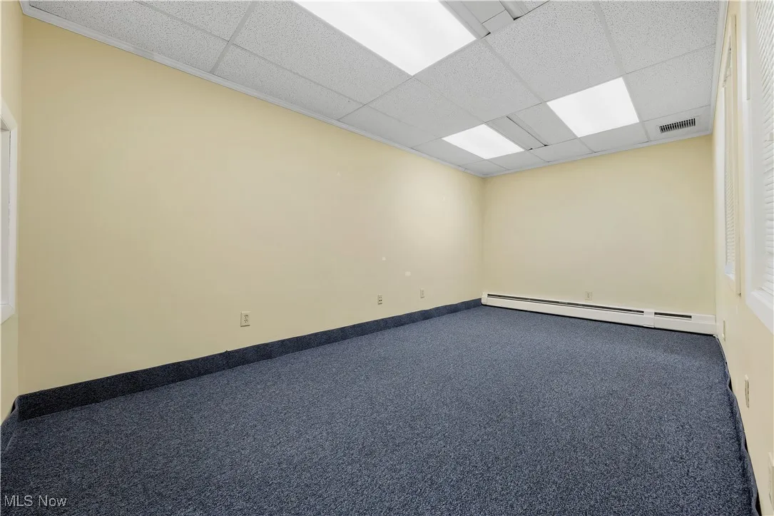 Unfurnished room with a baseboard heating unit, carpet, and a drop ceiling