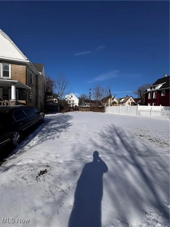 Snowy yard with a residential view and fence